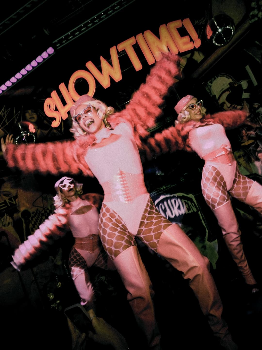 Dancers in pink costumes performing on stage under a “showtime” sign